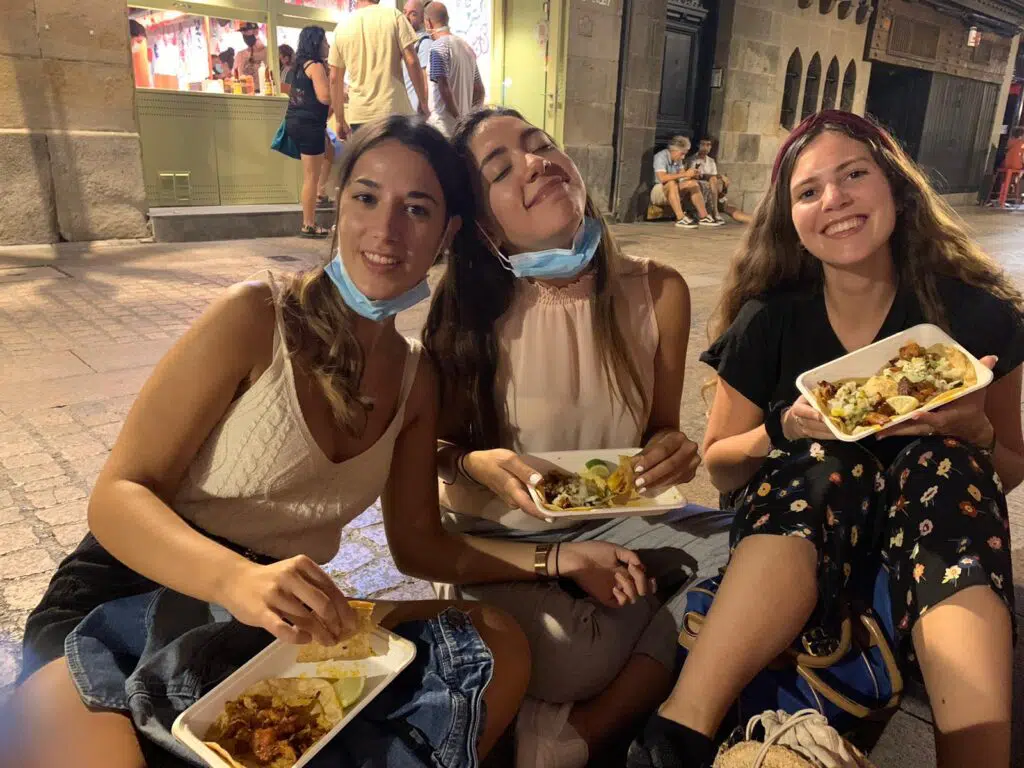 three English girls eating tapas while sitting in a street in Spain